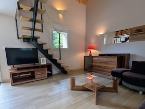 Ein modernes Wohnzimmer mit einem Glastisch, einem Flachbildfernseher, einer Holzunterhaltungsecke, einem dunklen Sofa, einer roten Lampe und einer Treppe mit Holzstufen.
