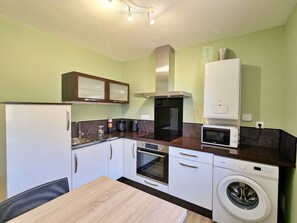 A compact kitchen with a refrigerator, microwave, oven, and washing machine.