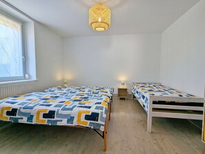 Un dormitorio con dos camas, una ventana con persianas, una lámpara colgante y una mesita de noche con lámpara.