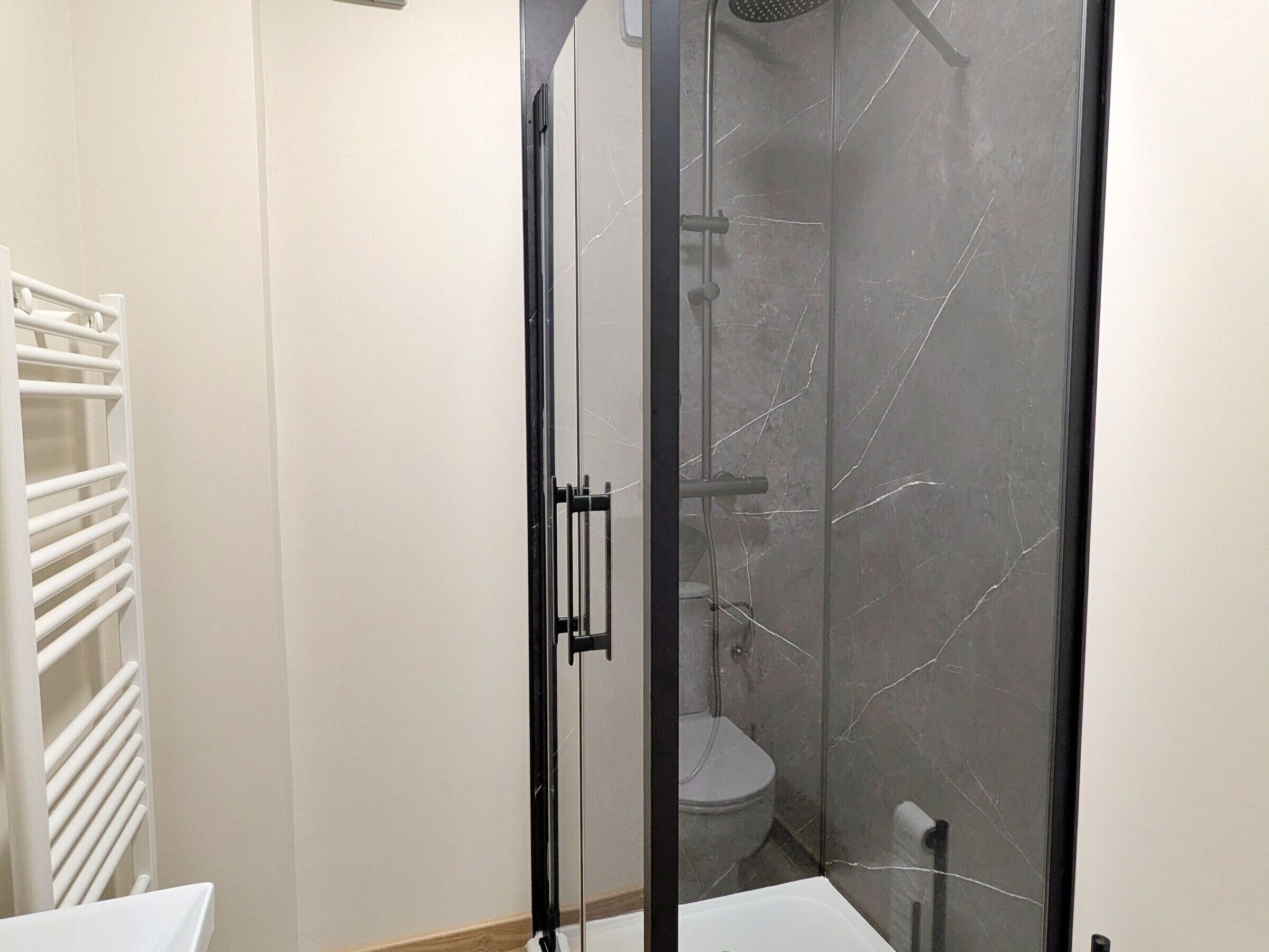 Un bagno con doccia vetrata, un water bianco e un porta asciugamani bianco.