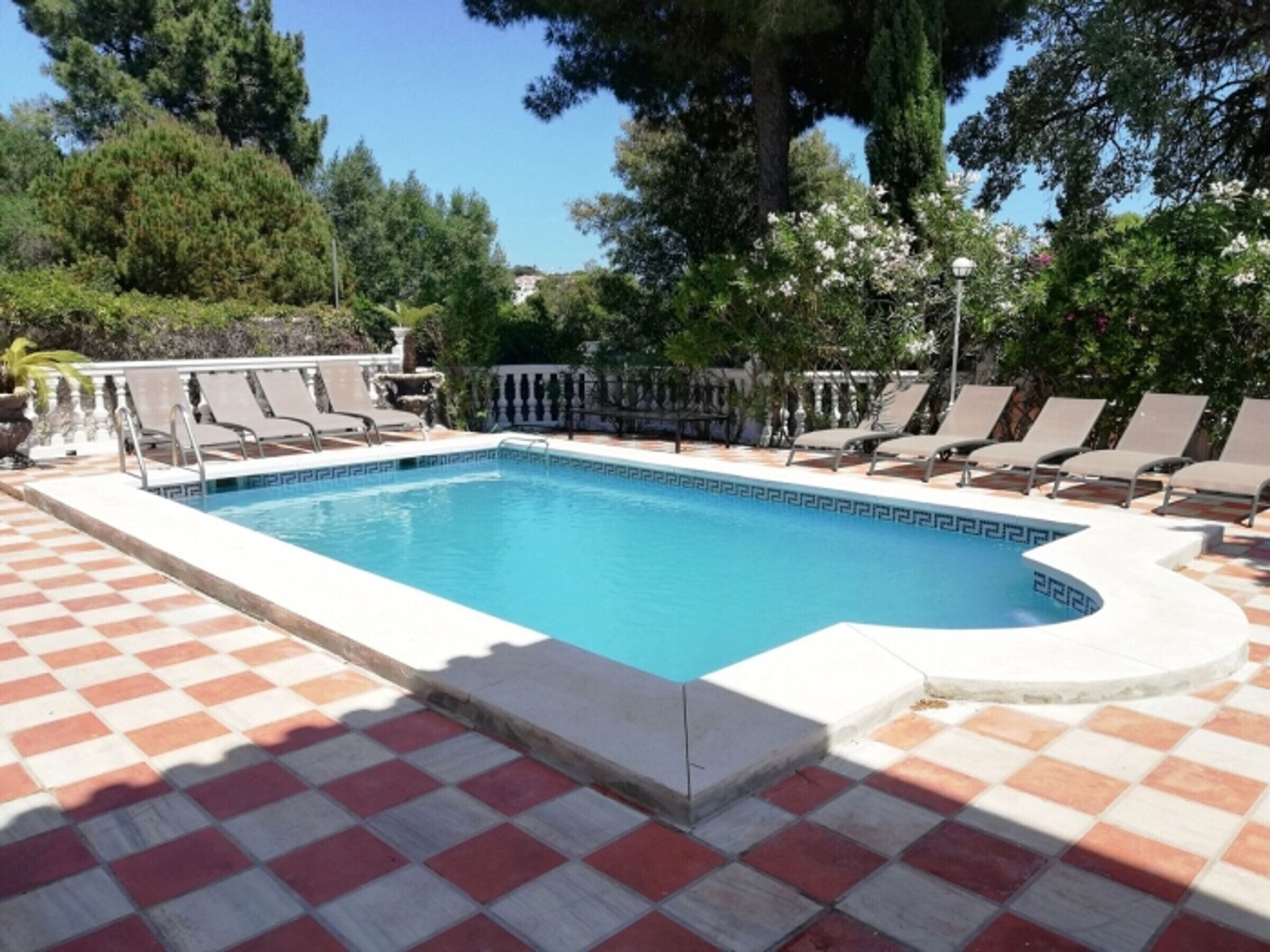 Ein rechteckiger Pool mit Schachbrettmuster, umgeben von Liegestühlen und einer niedrigen Mauer.