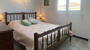 A bedroom with a wooden bed, two bedside lamps, a window, and a wall-mounted light fixture. - T2 apartment, clear view - 4 guests (Canet-en-Roussillon)