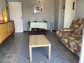 Ein Wohnzimmer mit einer Couch, einem kleinen Tisch, einer Kommode, einem gemusterten Teppich und einem an der Wand hängenden Bild.