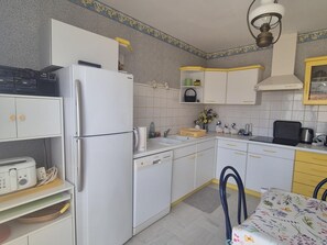 A kitchen with white cabinets, a refrigerator, a microwave, a sink, and a dining table with chairs. - Central apartment with balcony - 4 guests (Fouras)