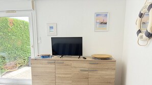 Une pièce avec un téléviseur posé sur un meuble en bois, une petite table et une vue sur la verdure à l’extérieur.