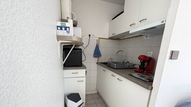 Une cuisine compacte avec des meubles blancs, une petite poubelle, une machine à café et un four à micro-ondes.