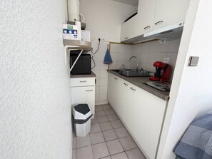 A compact kitchen with white cabinets, a small trash bin, a coffee machine, and a microwave. - T2 with private garden, calm - 4 guests (Saint-Georges-de-Didonne)