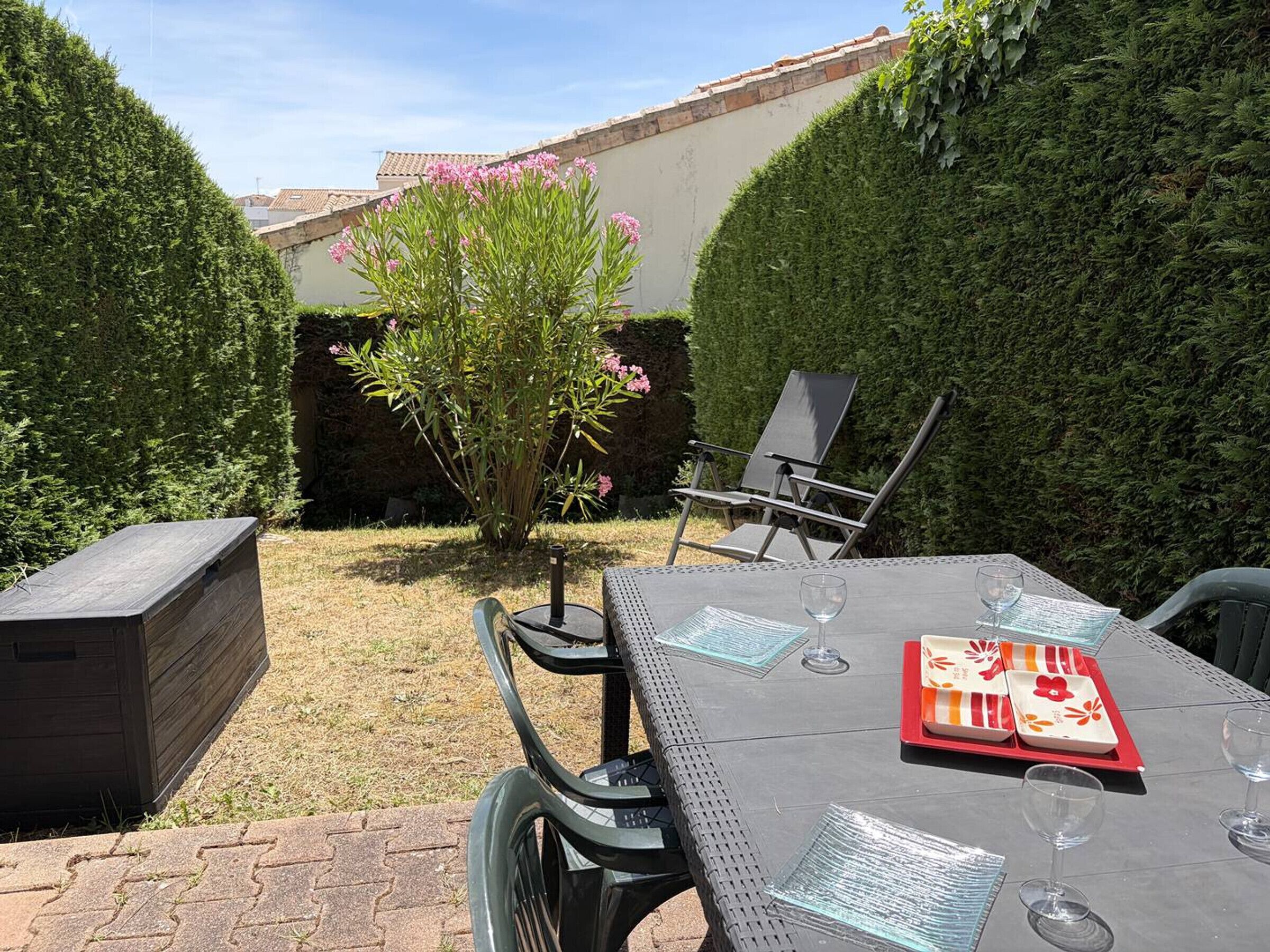 Patio esterno con tavolo apparecchiato per due, sedie e barbecue.