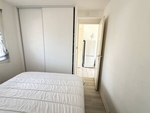 A bedroom with a bed, a wardrobe, and a door leading to a kitchen area. - T2 with private garden, calm - 4 guests (Saint-Georges-de-Didonne)