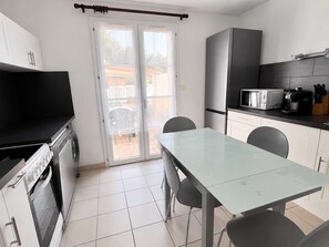 A compact kitchen with a dining area, a sliding glass door to the outside, and basic appliances. - House with AC, pool, parking - 5 guests (Argelès-sur-Mer)