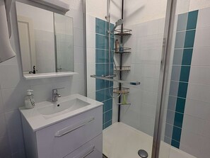 Een badkamer met een witte wastafel, spiegel en douche met blauwe tegels.
