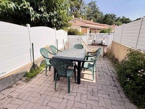 Een terras met tafel en stoelen, omringd door een witte hek en groen.