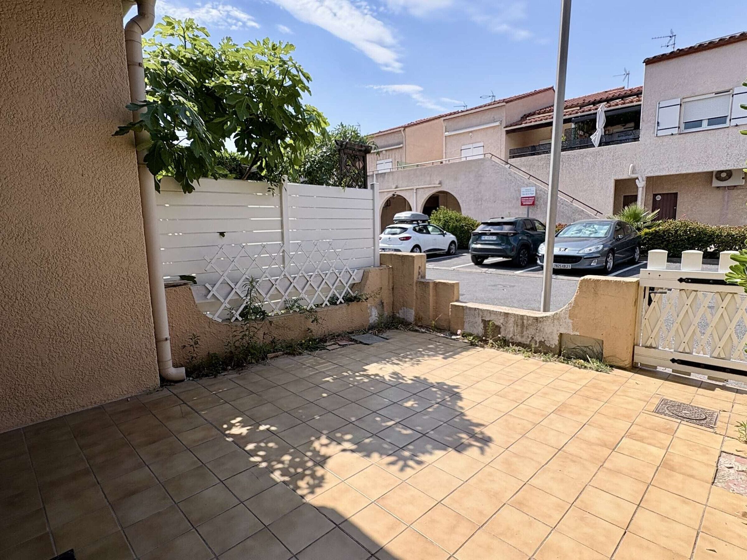 Zona residencial con patio empedrado, cerca de celosía blanca y coches estacionados.