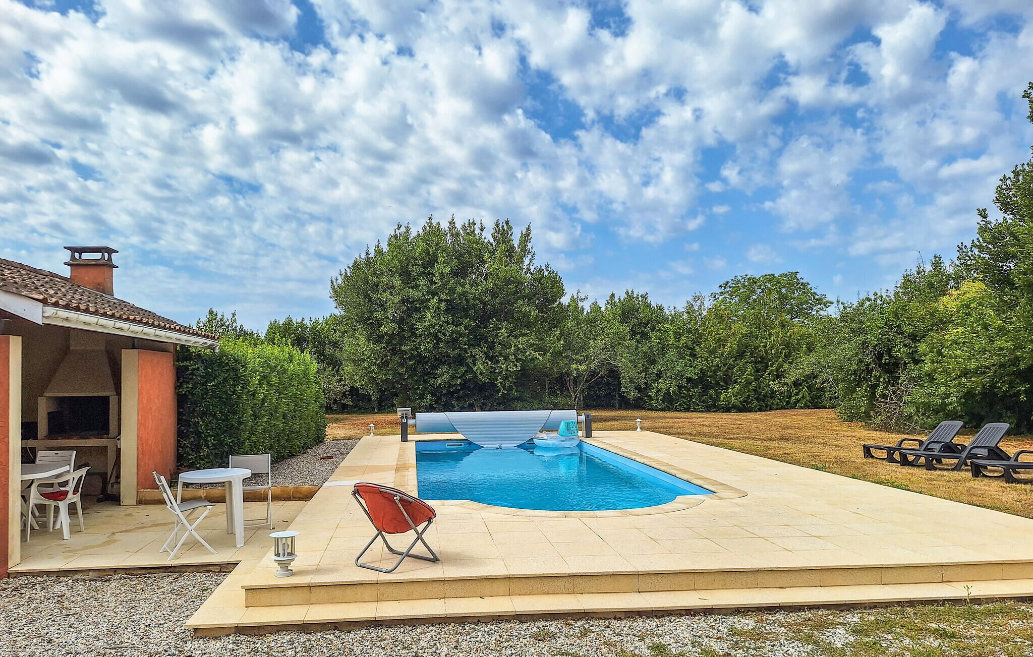Una piscina con solarium, mobili da esterno e una struttura coperta.