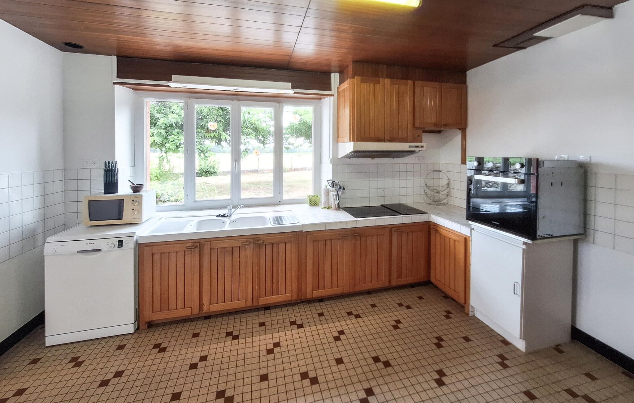 Una cocina con armarios de madera, microondas integrado, fregadero y refrigerador.