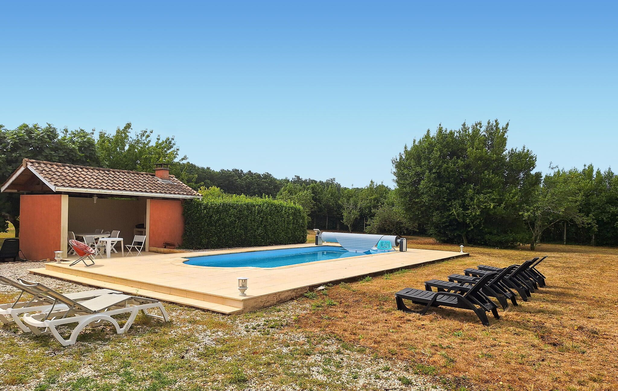A swimming pool with lounge chairs, a covered seating area, and a small building with a tiled roof.