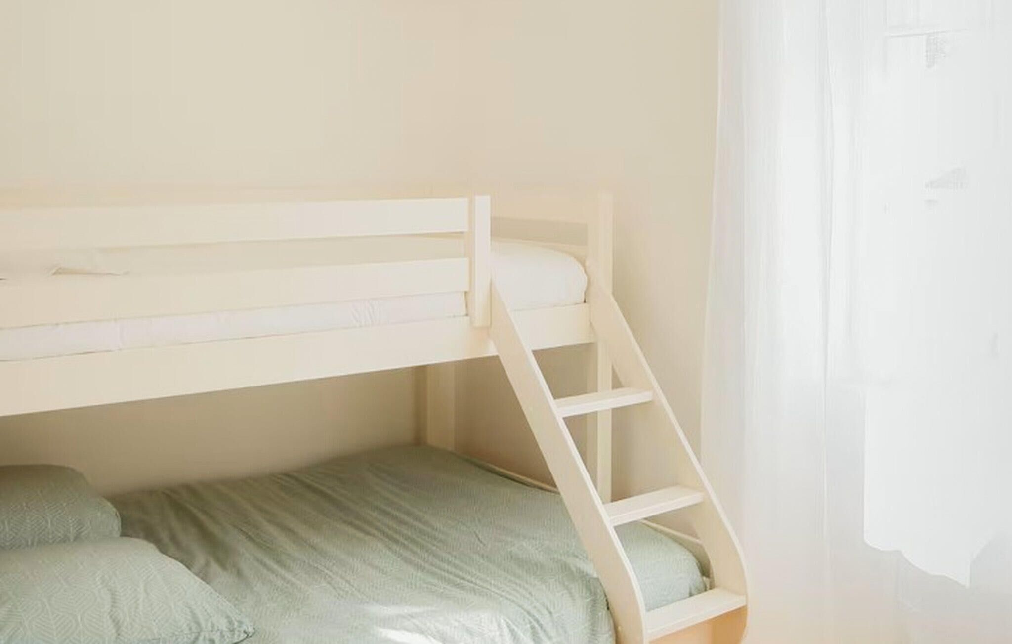 A bunk bed with a ladder, a single bed below, and a window with curtains.