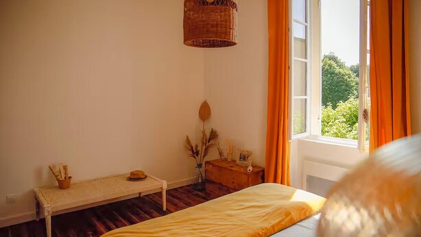 Ein Schlafzimmer mit einem Bett, einem Nachttisch, einem Fenster mit Vorhängen und einer Pendelleuchte.