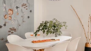 Ein Essbereich mit einem weißen Tisch, Stühlen, einer Pflanze und einer Wand mit Fischmotiven.