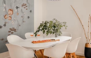 Ein Essbereich mit einem weißen Tisch, Stühlen, einer Pflanze und einer Wand mit Fischmotiven.
