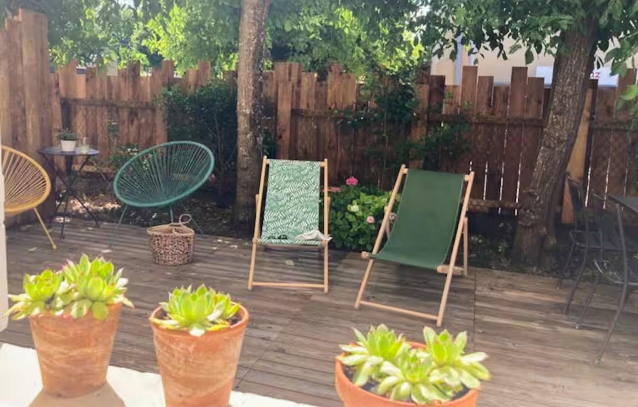 A wooden deck with two chairs and a table, surrounded by potted plants.