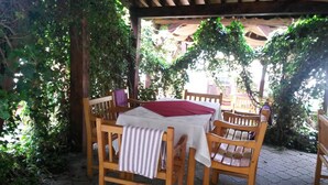 An outdoor wooden table with chairs, covered by a white tablecloth and a red napkin, surrounded by greenery. - Sighisoara Hotel (Sighisoara)