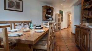 Una zona de menjador amb taula i cadires de fusta, cuina amb armaris de fusta i un quadre a la paret.
