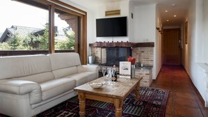 Un saló amb un sofà, una taula de centre amb gots i una ampolla, una llar de foc i un televisor muntat a la paret.