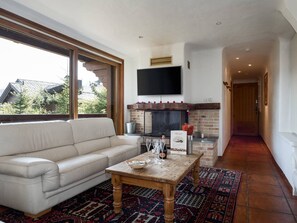 Ein Wohnzimmer mit einer Couch, einem Couchtisch mit Gläsern und einer Flasche, einem Kamin und einem an der Wand befestigten Fernseher.