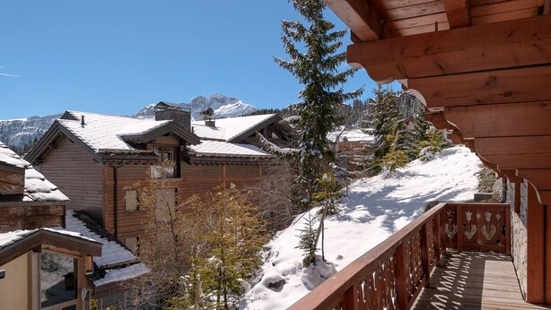 Una xalet de fusta amb un balcó que domina un paisatge de muntanya cobert de neu.