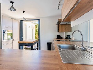 A modern kitchen with a wooden countertop, stainless steel sink, and built-in appliances. - Elegant house in nature - 6 guests (Saint-Clément-des-Baleines)