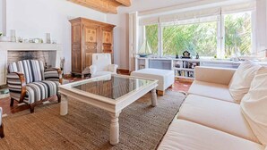 Amplia sala de estar con chimenea, un ventanal con vistas a zonas verdes y un rincón de descanso acogedor.