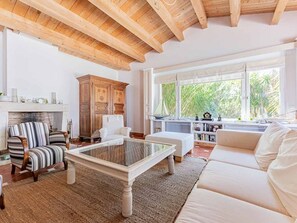 A spacious living room with a fireplace, a large window with a view of greenery, and a cozy seating area. - Elegant house in nature - 6 guests (Saint-Clément-des-Baleines)