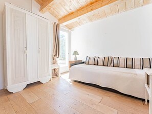 Et værelse med en seng, et skab, et vindue med gardiner og en lampe på et natbord.
