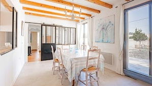 Un comedor con una mesa y sillas, vigas de madera en el techo, una araña y un ventanal con vistas.