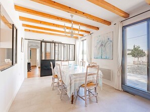 A dining area with a table and chairs, wooden beams on the ceiling, a chandelier, and a large window with a view. - Elegant house in nature - 6 guests (Saint-Clément-des-Baleines)
