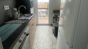 A compact kitchen with a sink, stove, and a view through the door. - Cross apartment with parking - 4 guests (Canet-en-Roussillon)