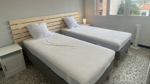A bedroom with two beds, a nightstand, a window with a view, and a radiator. - Cross apartment with parking - 4 guests (Canet-en-Roussillon)