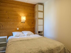 A bedroom with a wooden headboard, a bed with white bedding, a nightstand, and a wall-mounted light fixture. - Renovated apartment, ideal location - 6 guests (Plagne Bellecôte)