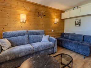 A modern living room with two sofas, a coffee table, and wooden paneling with wall-mounted lights. - Renovated apartment, ideal location - 6 guests (Plagne Bellecôte)