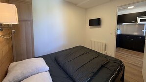 Un dormitori amb un llit, un armari de fusta, una televisió i una cuineta a l'habitació veïna.