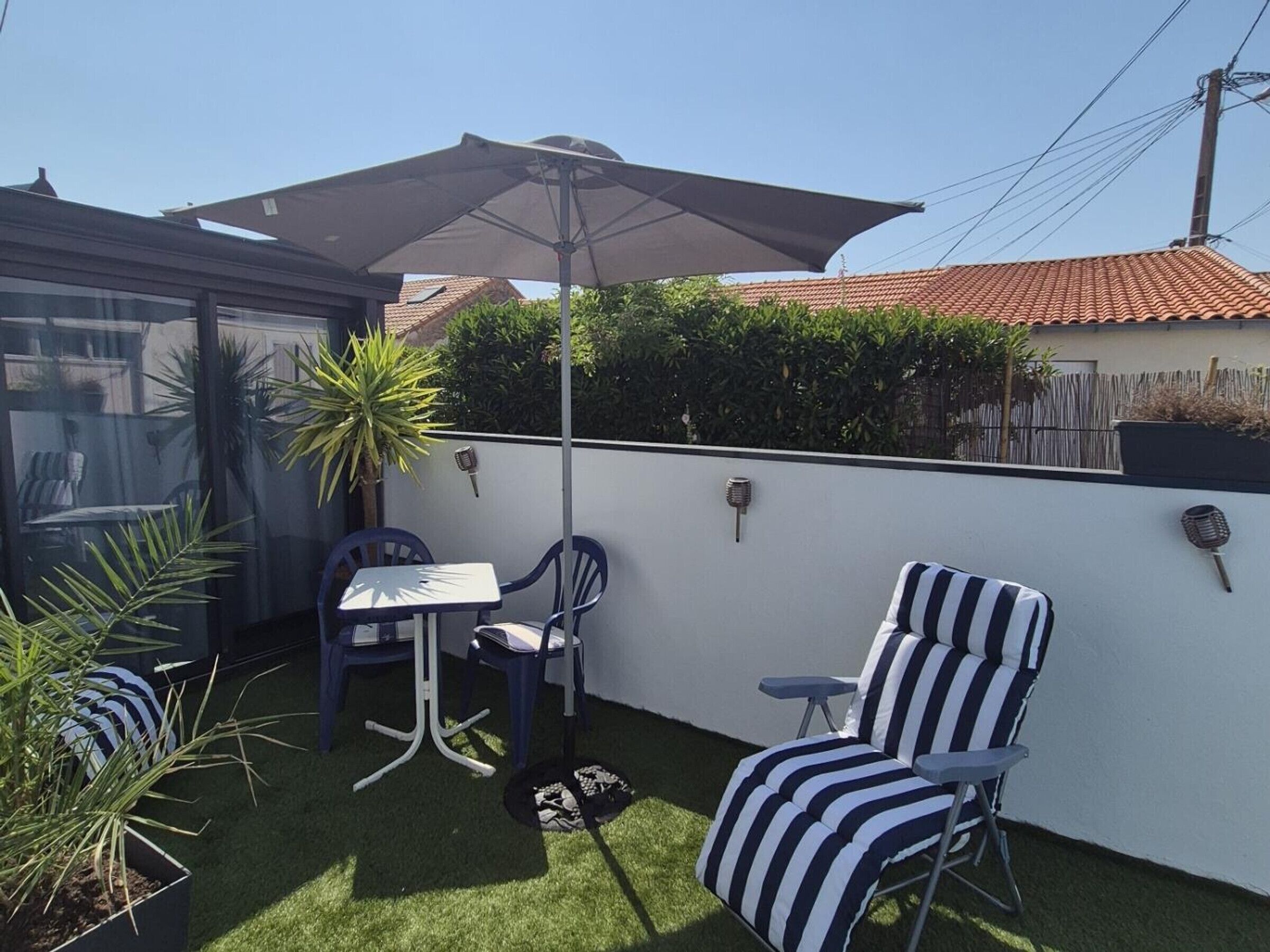 A patio with a table and chairs, a striped lounge chair, and a large umbrella.