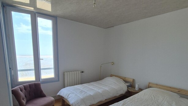 Slaapkamer met twee bedden, een stoel, een radiator en een raam met uitzicht.