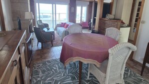 Een ruime kamer met houten plafond, een eettafel met stoelen, een bank en uitzicht door grote ramen.
