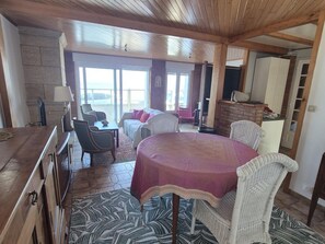 A spacious room with a wooden ceiling, a dining table with chairs, a sofa, and a view through large windows. - Charming house, sea view - 4 guests (Fouras)