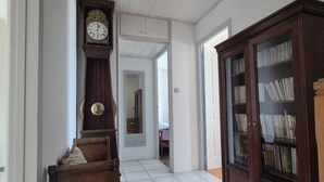 Een hal met een houten bank, een hoge staande klok, een spiegel en een boekenkast.