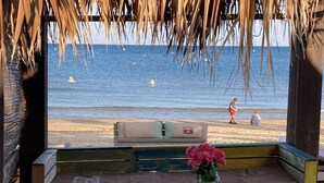 Un espace aménagé près de la plage, avec vue sur l’océan, comprenant un banc, une petite table et un vase rempli de fleurs.