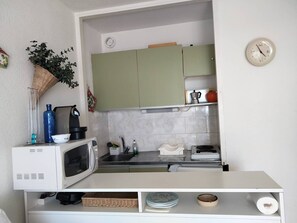 Eine kleine Küche mit Mikrowelle, Spüle und grünen Schränken.