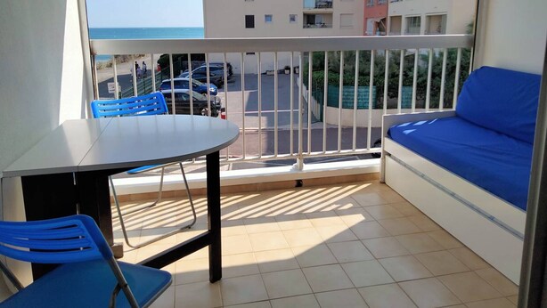 Un balcon avec une table et des chaises, un canapé et une vue sur un parking et des immeubles.