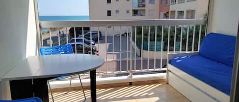 A balcony with a table and chairs, a sofa, and a view of a parking area and buildings.